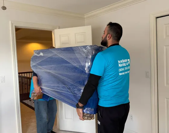 Mover carrying wrapped bedroom furniture out of a home