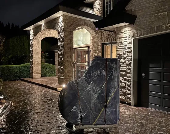 A grand piano fully wrapped and staged on a dolly in a home driveway